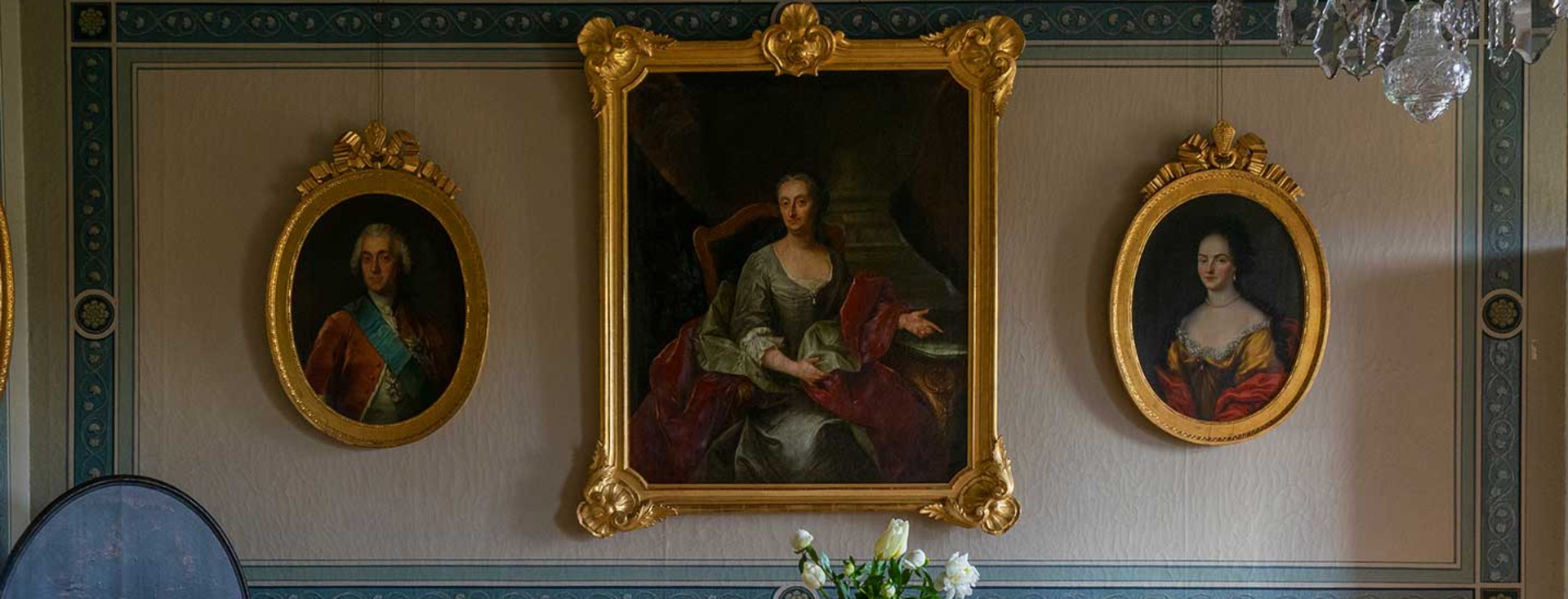 Ett slottsrum i beige och blått med flertalet stora porträtt.
